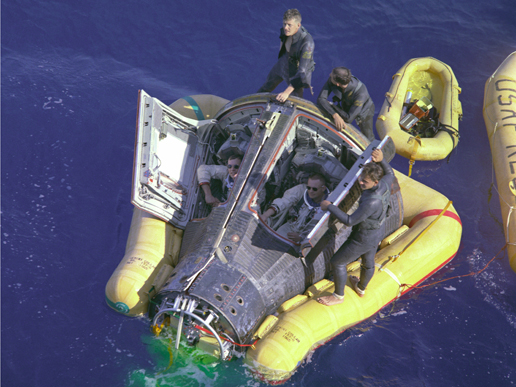 Astronauts Neil Armstrong and David R. Scott, assisted by U.S. Navy divers, await the arrival of the recovery ship after completion of their Gemini 8 mission.
