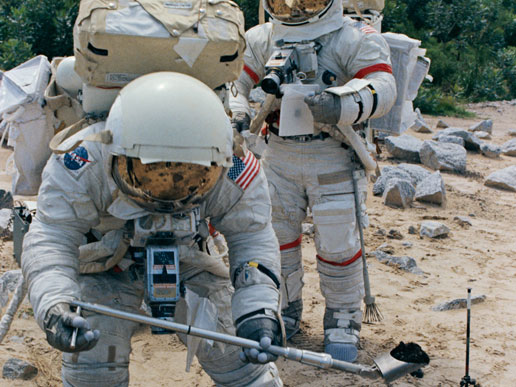 Harrison H. Schmitt (foreground), lunar module pilot, simulates scooping up lunar sample material. Mission commander, astronaut Eugene A. Cernan, is in the background.